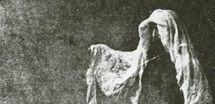 Black and white photo of a ghostly figure draped in cloth, evoking mysterious events and urban myths.