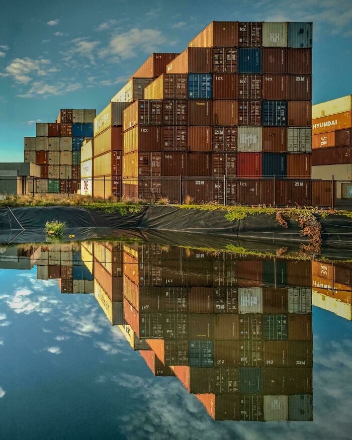 Stacked shipping containers reflecting in water under a blue sky, creating a satisfying picture for a gentle reset.