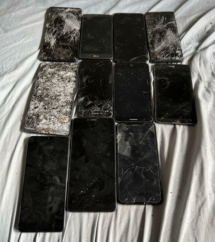 A collection of old, severely damaged smartphones with cracked screens and dirt, representing a red flag in technology.