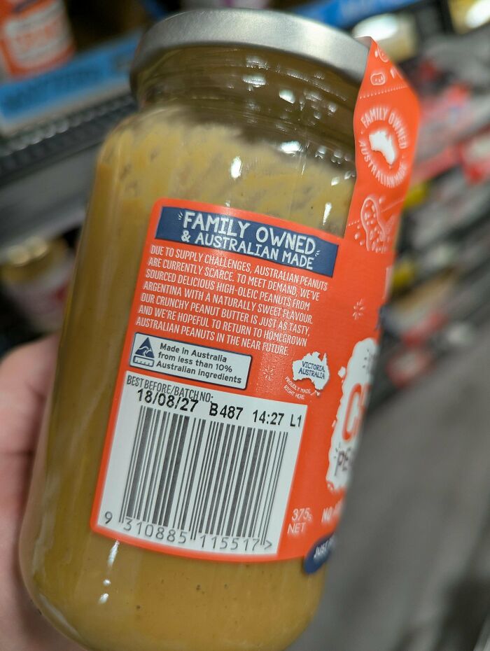 A hand holding a jar of Australian made peanut butter, showcasing the label and barcode for an Aussie audience.