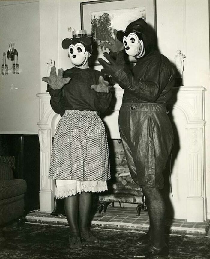 Two people wearing vintage cartoon character costumes standing indoors by a fireplace in a trashy wedding story.