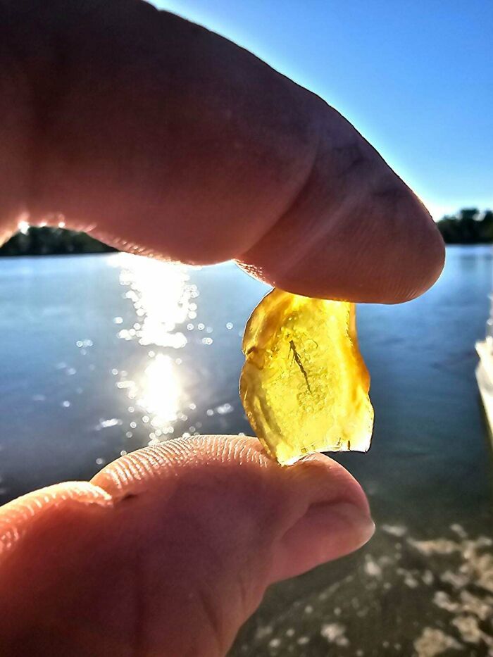 Fingers hold a small, translucent yellow unusual possession with an inclusion against a sparkling water backdrop.