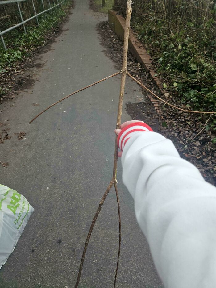 Person in a white sweatshirt holding a stick resembling a human figure on a paved path. Relatable memes for playful minds.