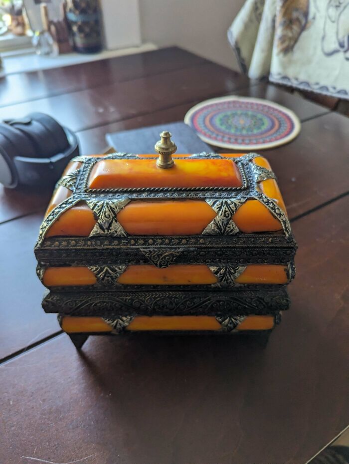 An antique orange and silver box with intricate designs, an unusual possession, sits on a wooden table.