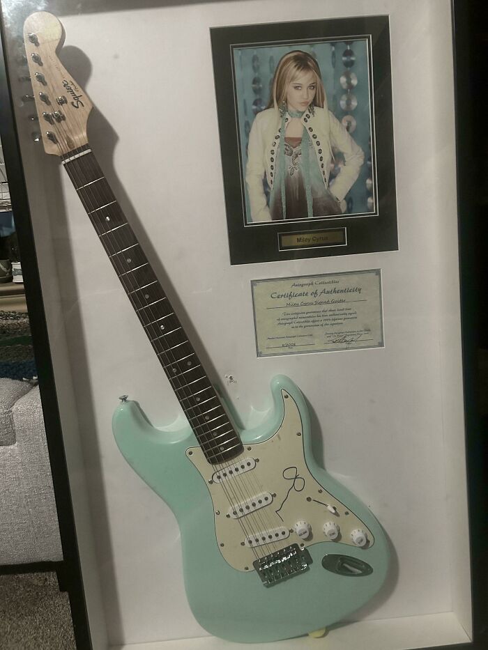 Framed light blue Squier guitar with a Miley Cyrus signature, photo, and certificate, showing the value of unusual possessions.