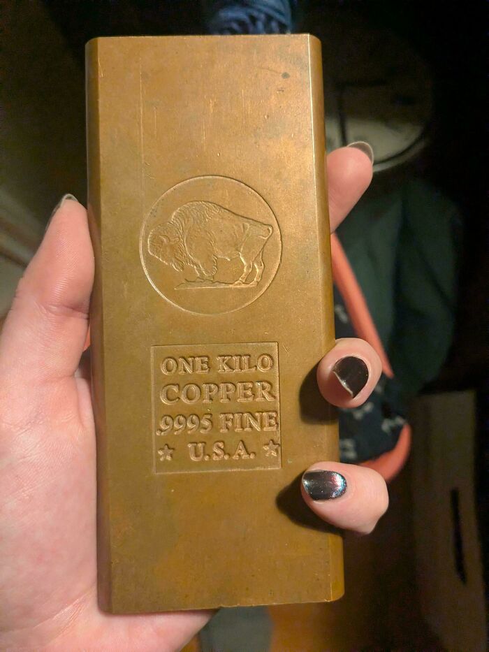 A hand holds a 1-kilo copper bar. It features a buffalo design and text, highlighting the value of unusual possessions.