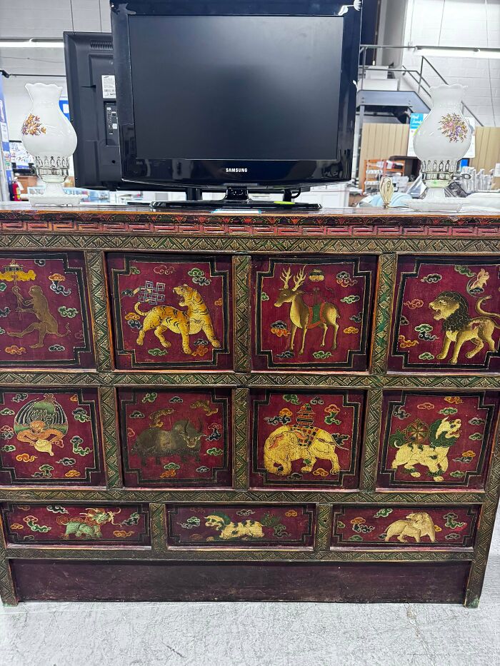 An intricately painted chest, displaying various animals, an unusual possession, below a modern TV and lamps.