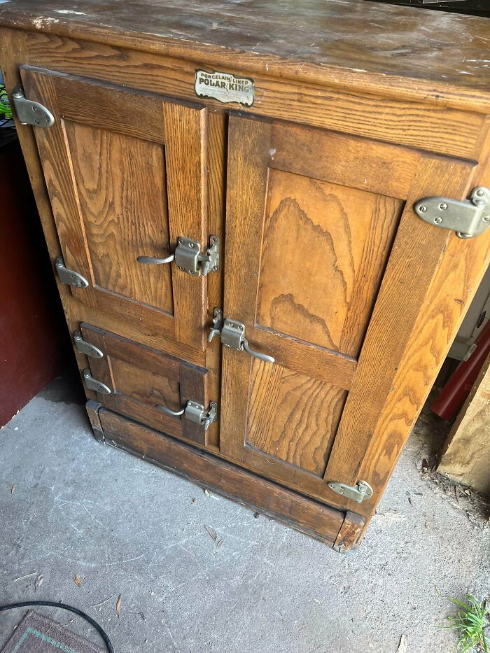 An old wooden refrigerator, labeled Polar King, with metal latches on its doors. An unusual possession with true value.