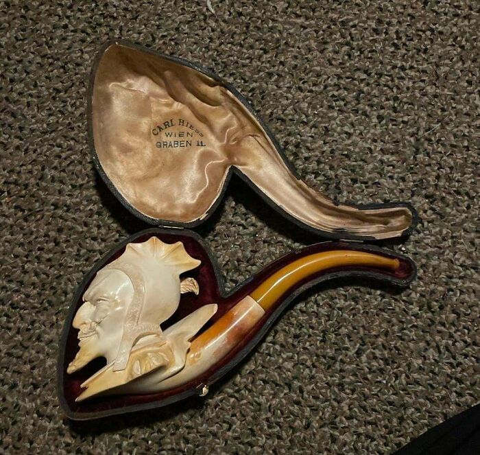 A vintage pipe with an intricate carved face, lying in its velvet-lined case, showcasing the unusual possessions true value.
