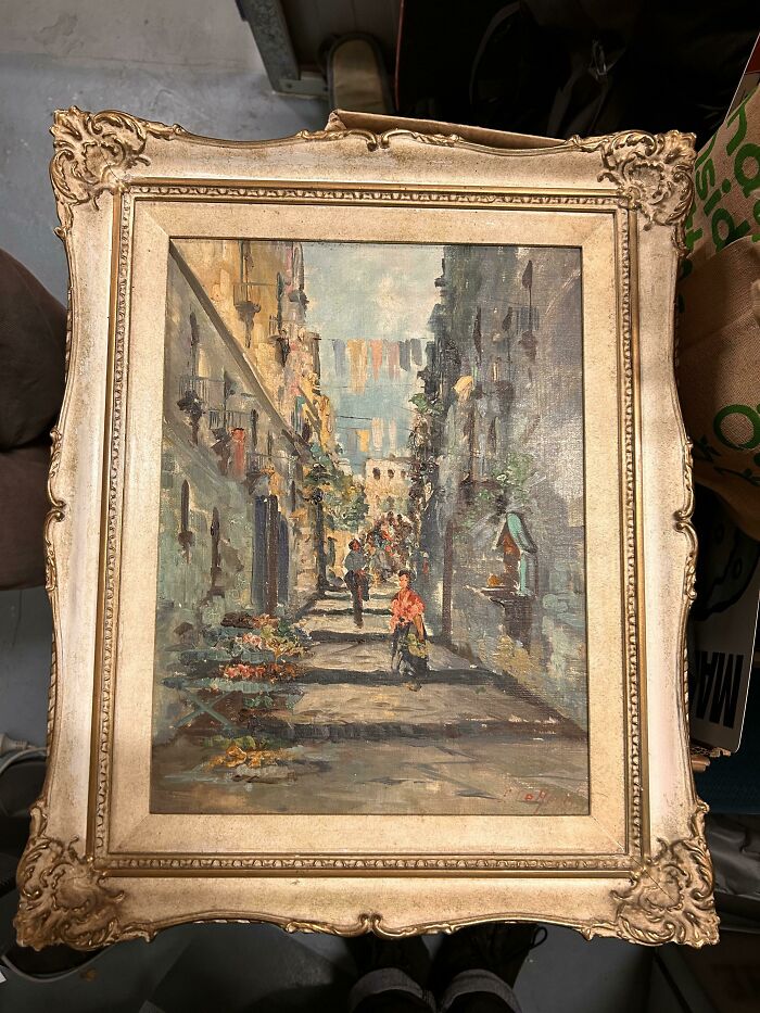 An oil painting depicting a European street scene with people and clotheslines, an unusual possession in an ornate frame.