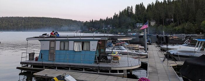 A vintage houseboat docked with other boats. A person sits on the roof, enjoying the unusual possessions.