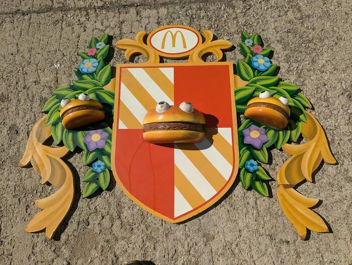 Unusual possessions: A decorative McDonald's crest featuring googly-eyed hamburgers and floral embellishments against a concrete wall.