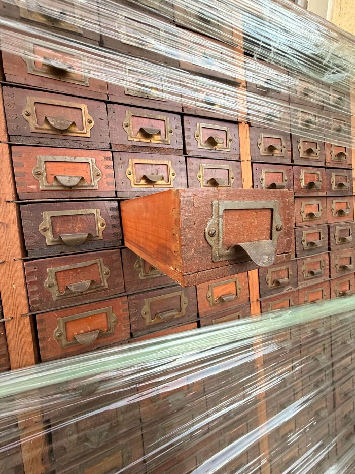 A large collection of small, wooden drawers with metal handles, stacked and wrapped in plastic. One drawer is slightly open, showing its true value as an unusual possession.
