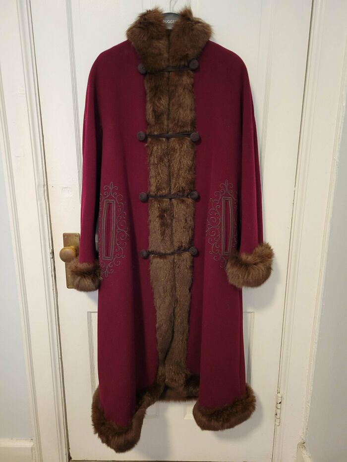 A vintage burgundy coat with brown fur trim, hanging on a white door. Its unusual possessions and design show true value.