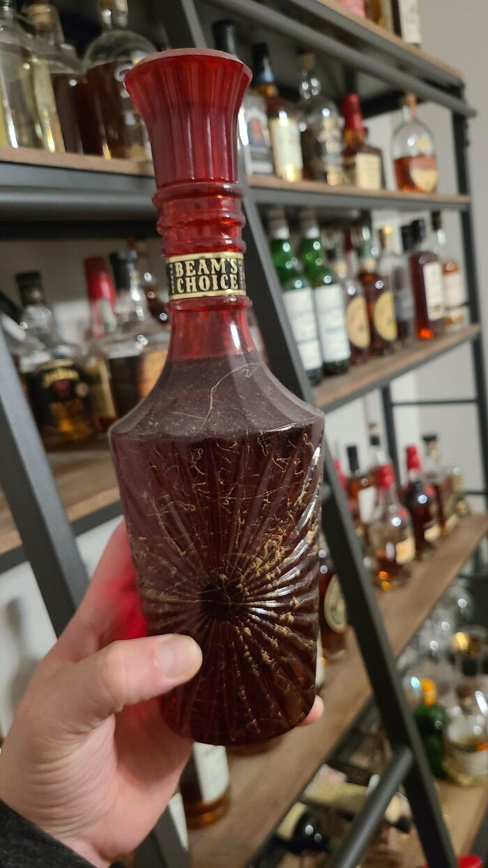 A hand holds a vintage red glass Beam's Choice bottle with unusual etched details, revealing its true value.