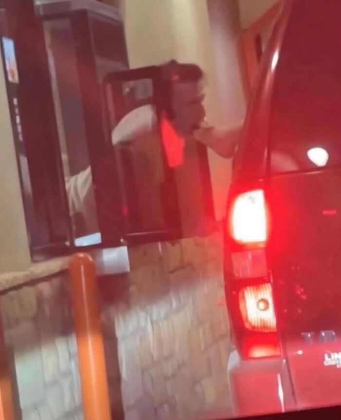 A man leaning out of a car window, distorted by red light, creating a weird image at a drive-thru.