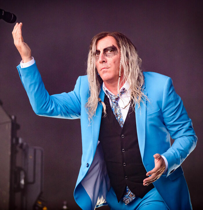 Maynard James Keenan performing on stage in a bright blue suit with distinct black eye makeup.