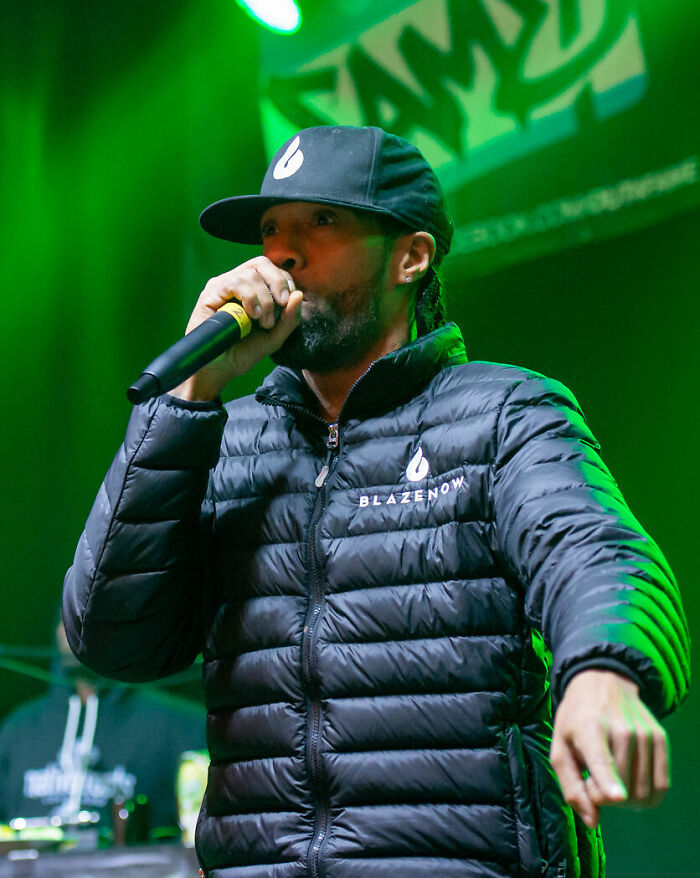 Redman performing on stage wearing a black jacket and cap, engaging the audience with a microphone in hand.
