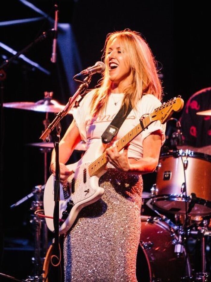 Liz Phair performing live on stage, playing electric guitar and singing passionately during a concert.