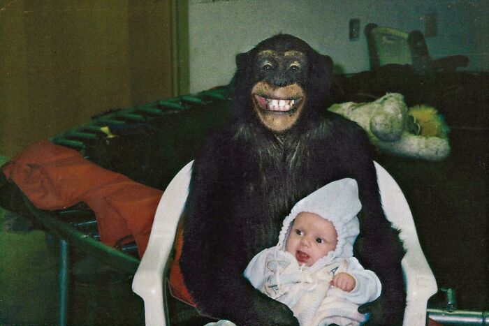 A creepy image of a person in a realistic chimpanzee mask holding a baby, part of "Creepy Images You Should View At Your Own Risk".