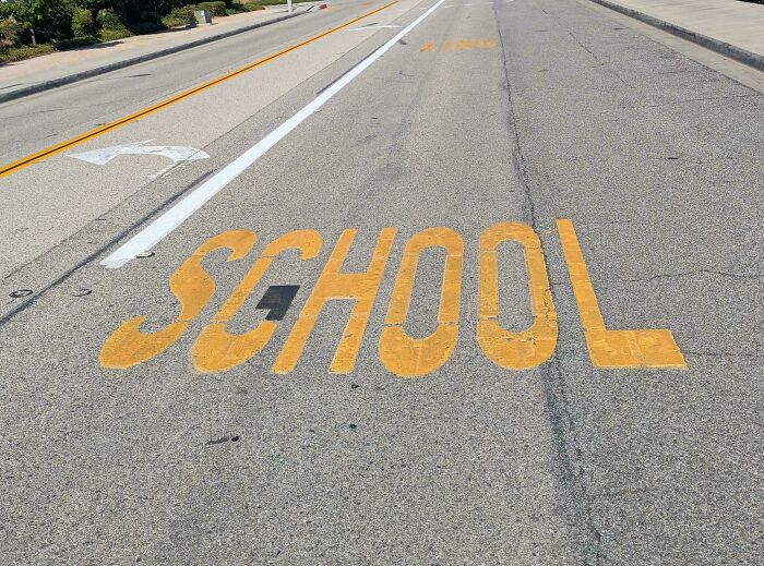 The word SCHOOL painted on an asphalt road with a letter L partially obscured by a pothole, a funny fail.