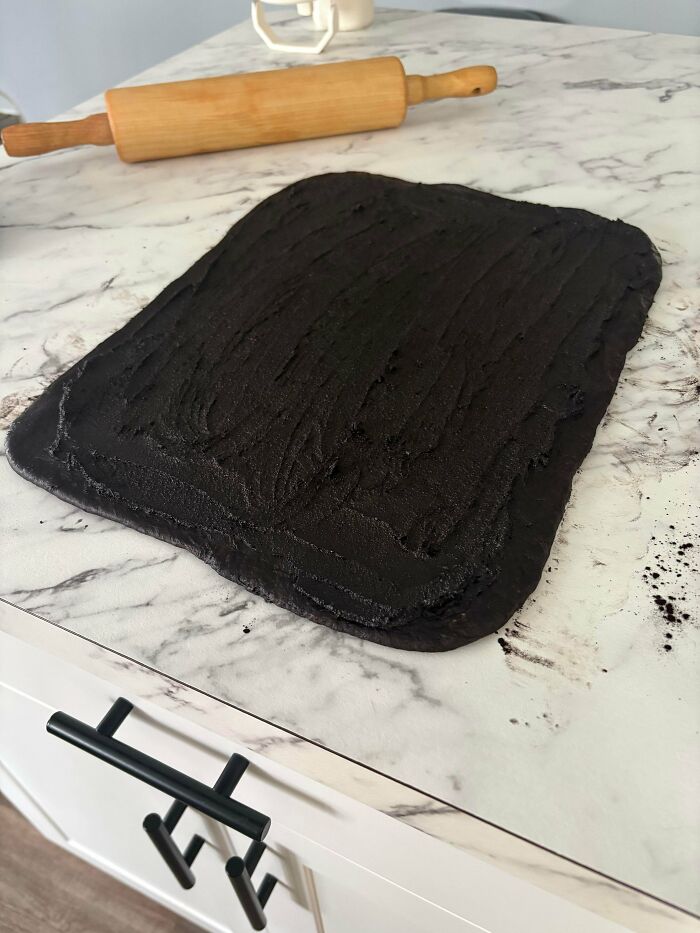 Black dessert dough rolled out on marble countertop with wooden rolling pin