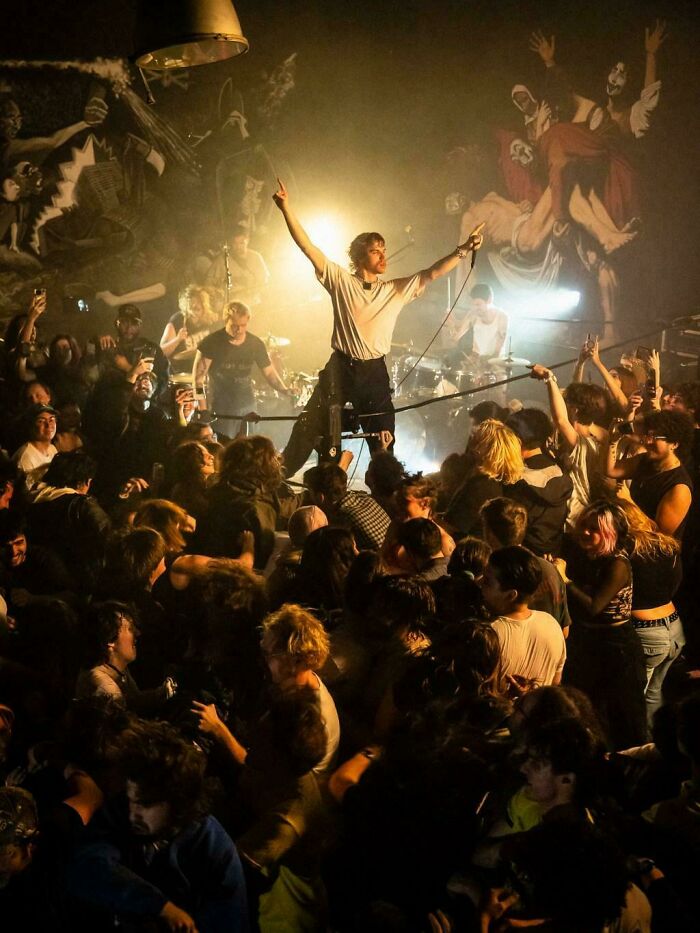 A lead singer with arms raised in a crowded concert, capturing an Accidental Renaissance aesthetic.