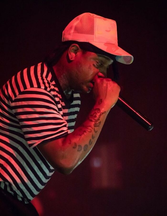 Ski Mask the Slump God performing on stage wearing a striped shirt and white cap, holding a microphone close to his mouth.