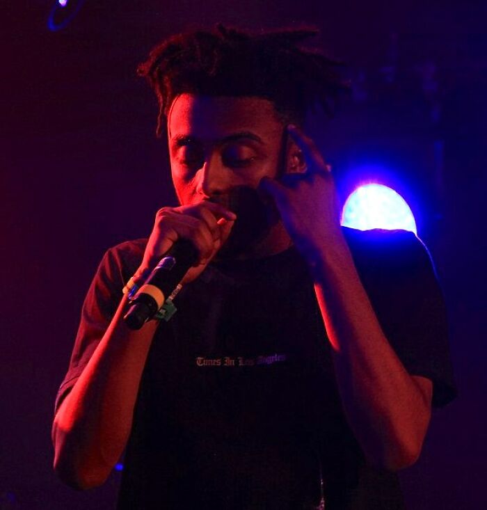 Amin&eacute; performing on stage under red and blue lights, holding a microphone close to his mouth.