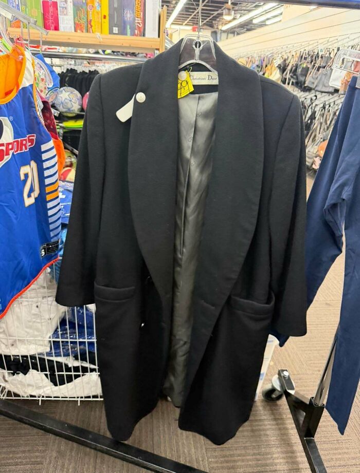 A black Christian Dior coat, a high-fashion thrift store jackpot find, hanging in a retail setting.