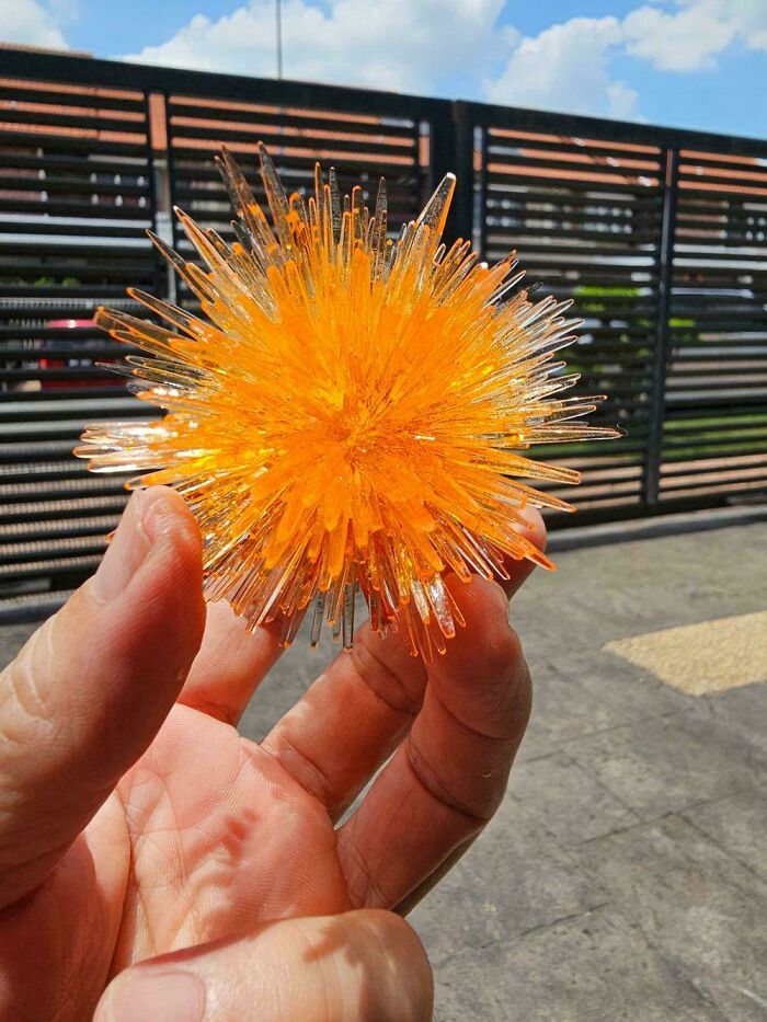 A hand holding an orange, spiky, star-shaped object, a handmade project demonstrating patience and skill.
