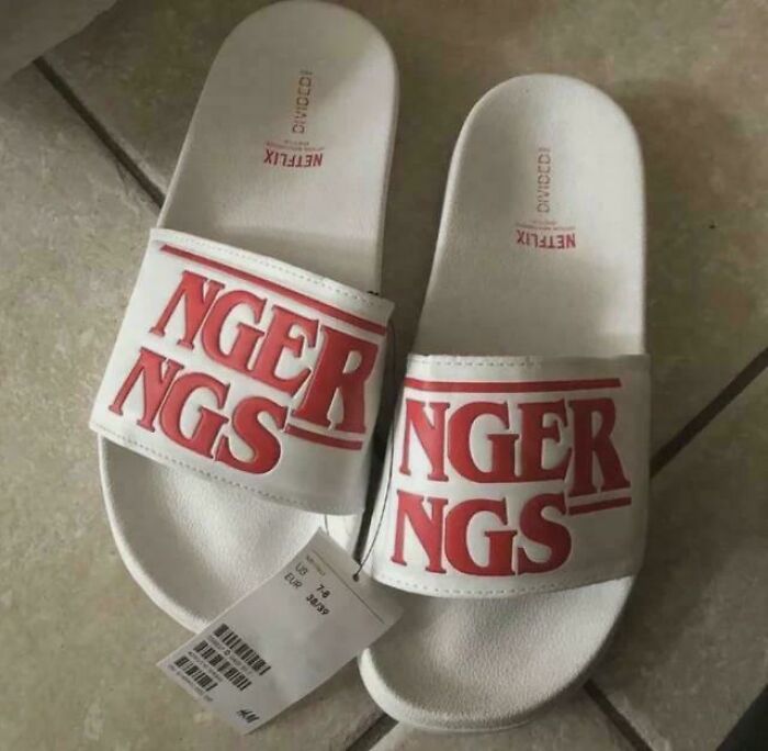 A pair of white slide sandals with the word NGERNGS printed in red, a funny fail trying to spell Stranger Things.