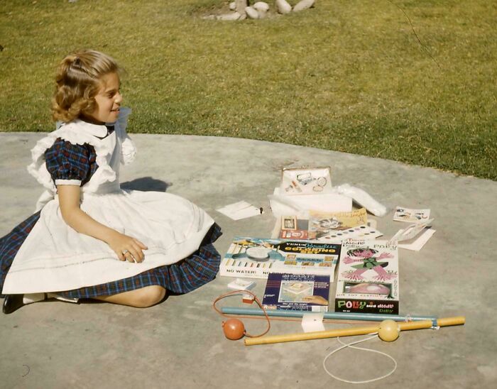 Candid old photo of a young girl sitting on the ground with her new toys and games, looking excited.