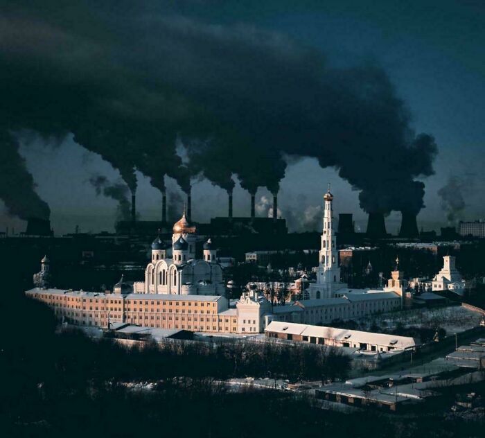 Industrial factory emitting smoke behind church in urban hell
