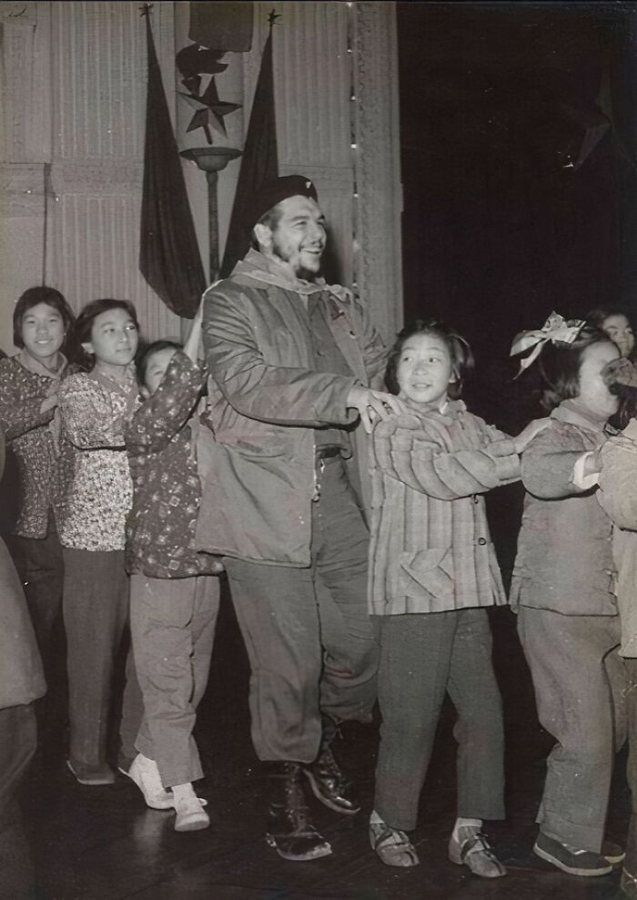 Black and white historical photo of a man and children holding hands in a playful line, representing a vastly different world.