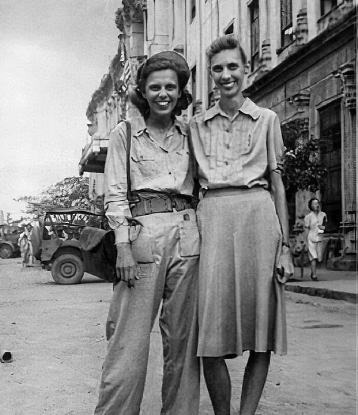 Two women smiling on a street wearing 1940s clothing in a historical photo representing a vastly different world.