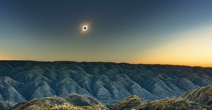 Unbelievable photos: a total solar eclipse over layered mountains with a vibrant sunset sky. Glimpses into another universe.