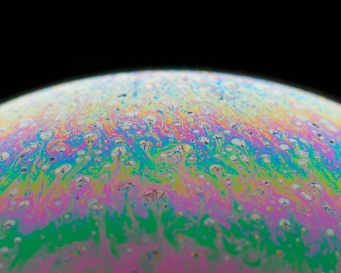 Unbelievable photos of a macro shot of a soap bubble surface, showcasing swirling iridescent colors that feel like another universe.