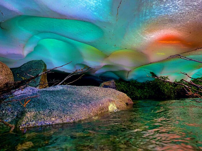 Unbelievable photos taken on Earth: A vibrant ice cave with glowing colors above a clear stream and rocks.