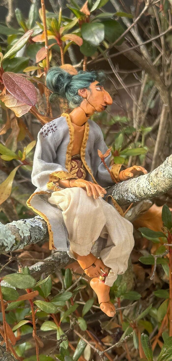 A handmade doll with green hair and clothes sitting on a tree branch, highlighting handmade projects.