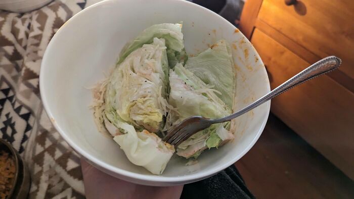 A white bowl with iceberg lettuce, dressing, and a fork, suggesting a simple meal or a Bananasausage food crime.