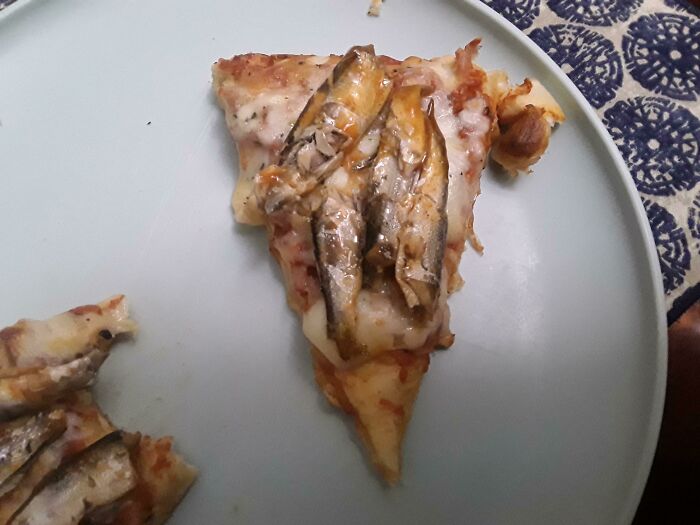 A pizza slice topped with whole fish, a "Bananasausage" food crime that needs a priest.