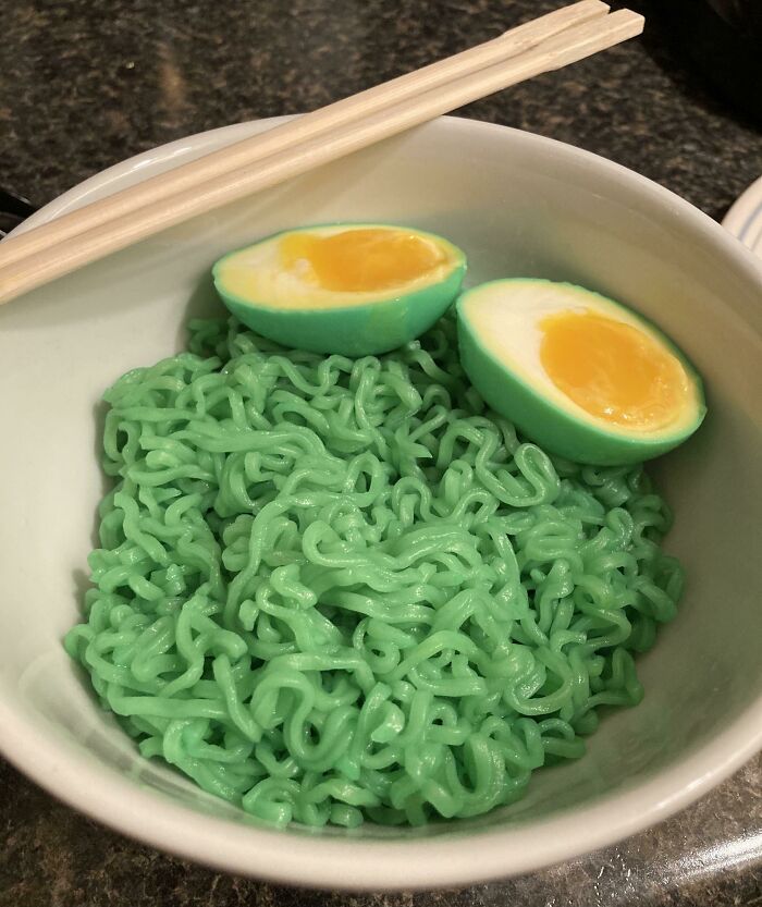 A bowl of bright green noodles with two vivid green halved soft-boiled eggs, displaying Bananasausage food crimes.