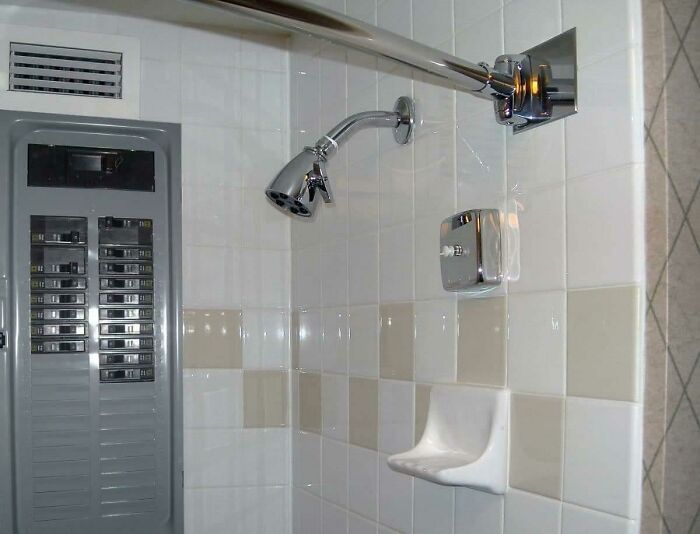 A disastrous home improvement fail: an electrical panel next to a shower, a major safety hazard. Concrete overflowed out of the toilet.