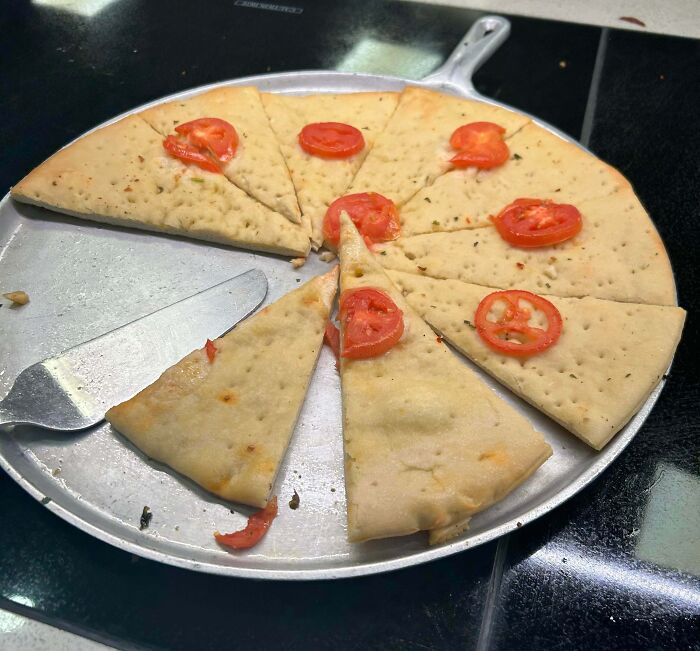 A plain pizza with a few tomato slices, some pieces already taken. A bananasausage food crime.