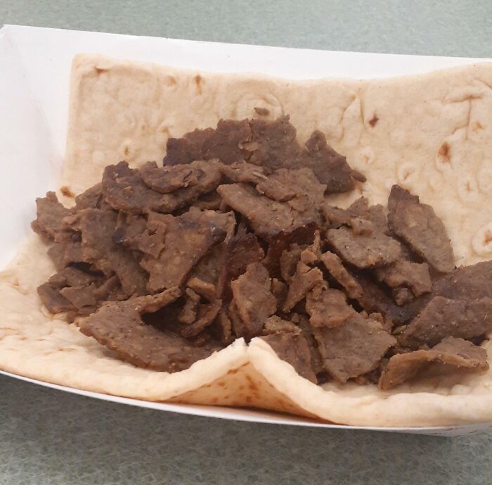 A pita bread filled with brown, thinly sliced meat, resembling a Bananasausage or another food crime.