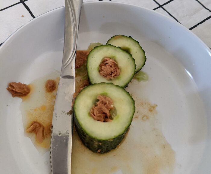Sliced cucumber filled with tuna on a white plate with a knife, a bananasausage food crime.