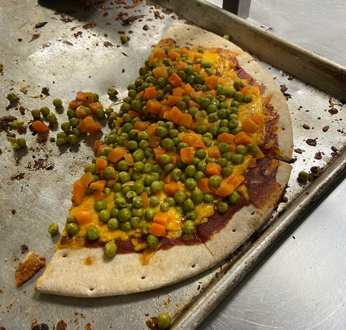 A Bananasausage pizza topped with bright green peas and orange diced carrots on a baking sheet, a true food crime.