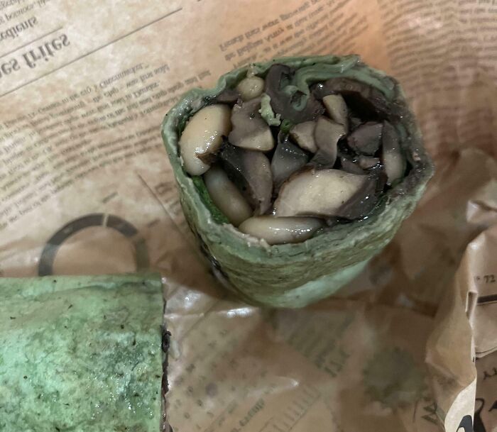 A questionable green Bananasausage wrap overflowing with mushrooms and white beans on crumpled paper.