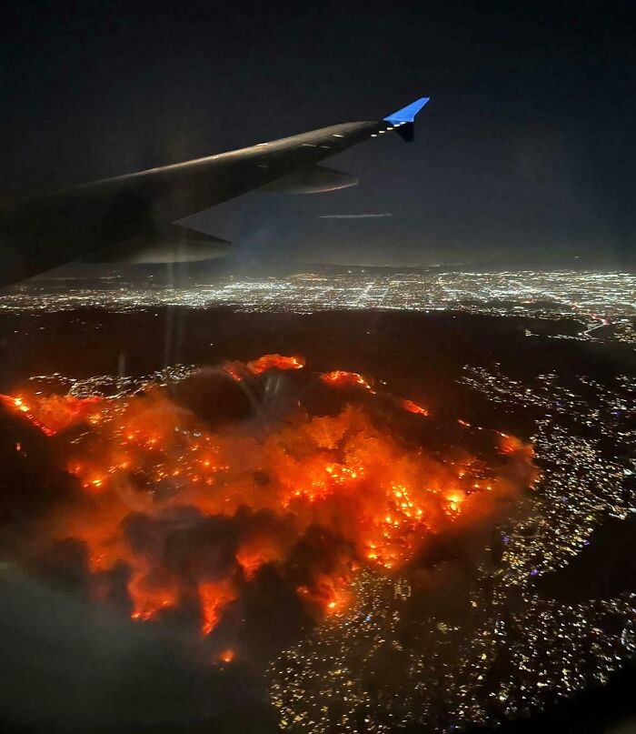 Aerial view of a fiery landscape at night resembling a devil sunrise with city lights in the distance.